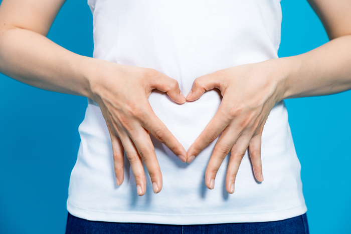 Woman forming heart shape with hands. Prioritize digestive health with our strategies for bloating and constipation relief.