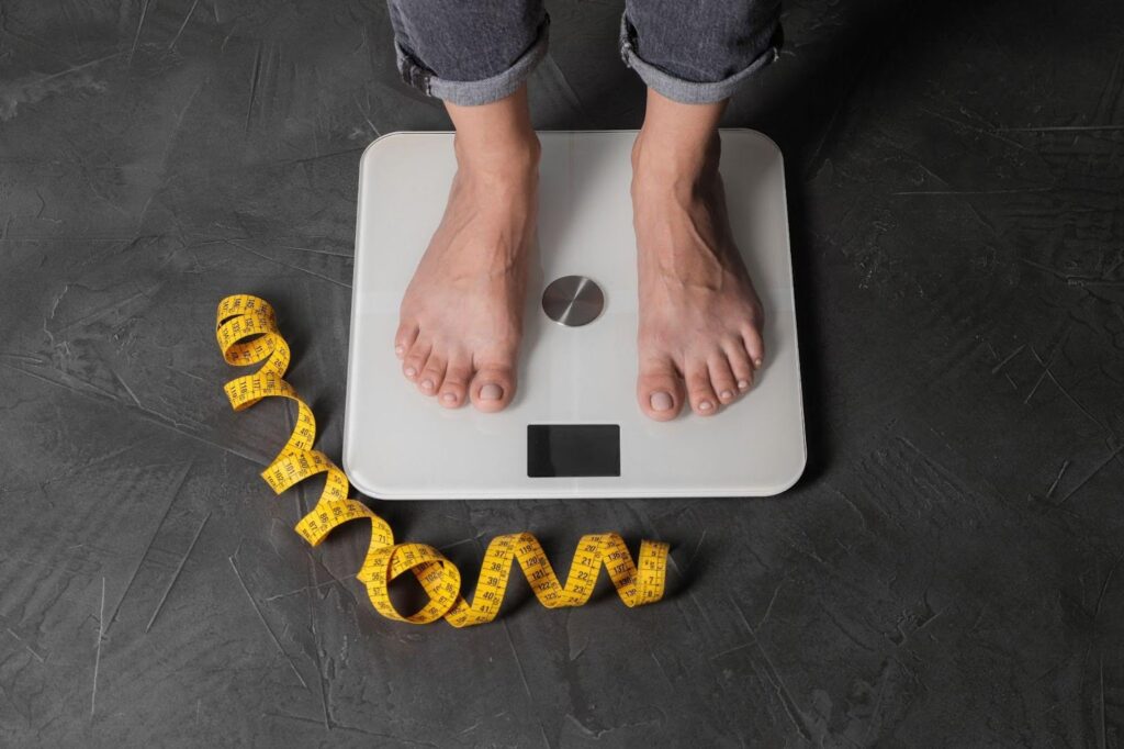 Individual on a scale, measuring their weight while holding a tape measure for body measurement