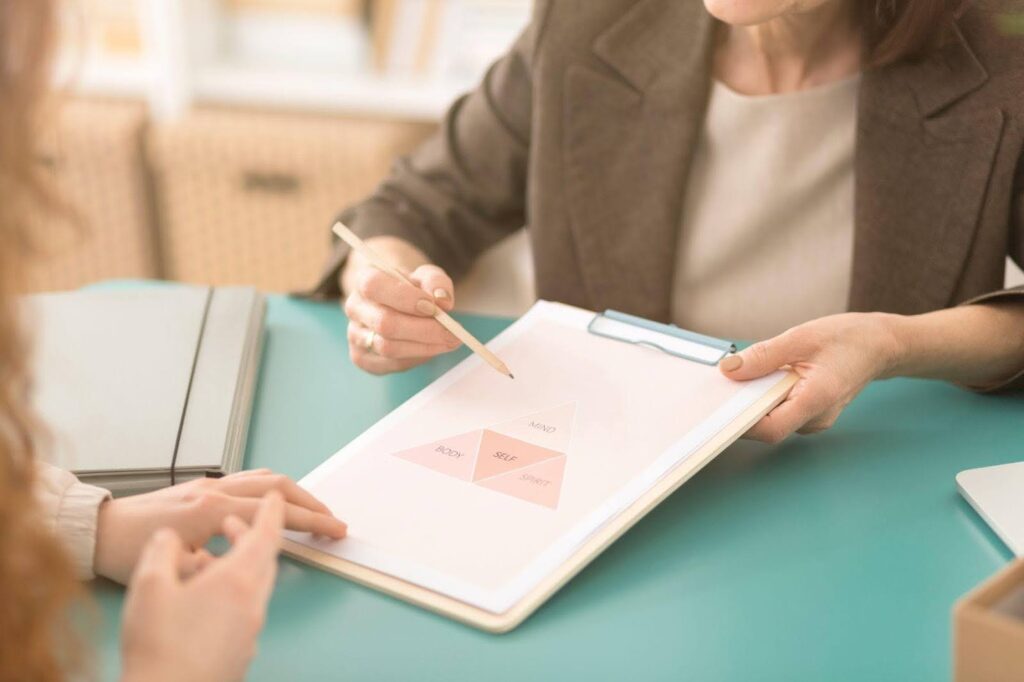 A woman diligently writes on a clipboard, with another woman observing her process nearby