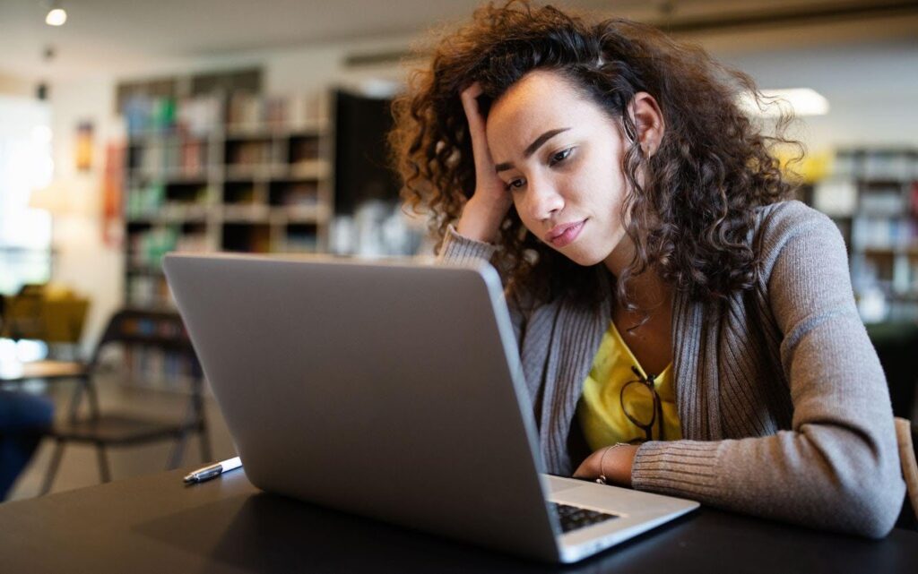 A woman supports her head with her hand, contemplating her laptop at the table