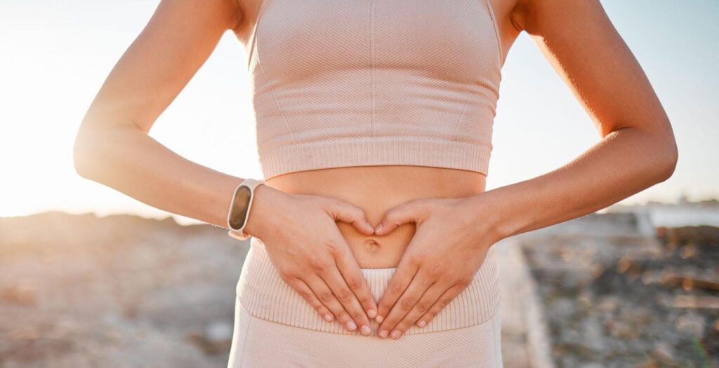 A woman gently holds her stomach with both hands appearing contemplative or in discomfort