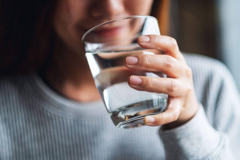 A woman with a cheerful expression holding a glass of water in her hand