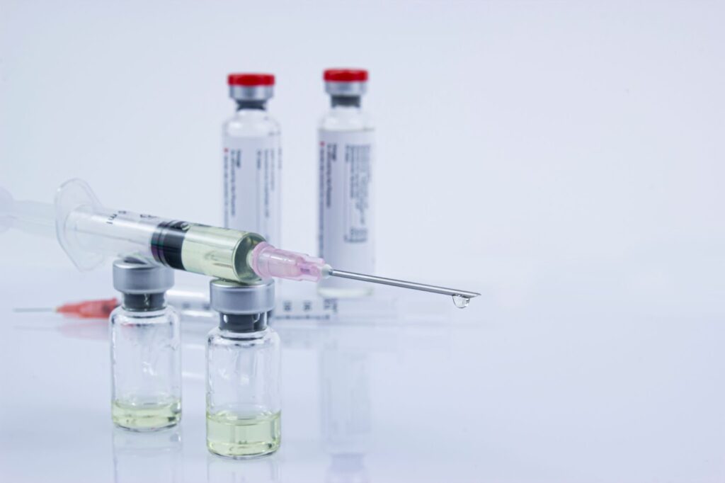 Syringe and vials with yellow liquid on a light background.