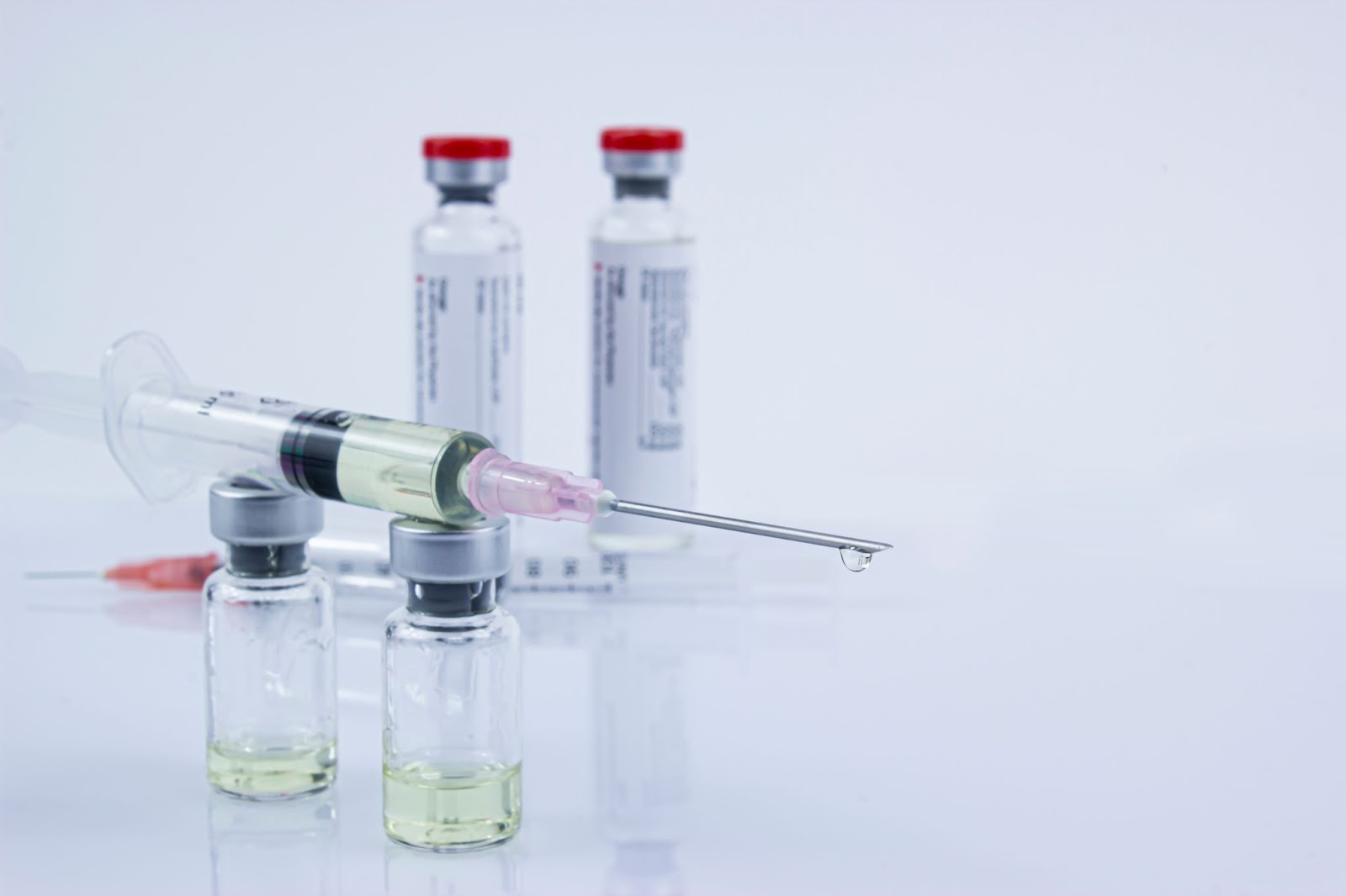 Syringe and vials with yellow liquid on a light background.