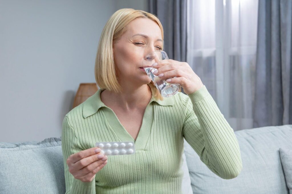 A woman sits on a couch sipping water from a glass looking relaxed and comfortable in her living room